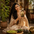 Woman holding a bottle of Kesh Sneha hair growth toner ingredient's details   in a traditional setting with plants and bowls.