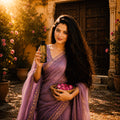 Woman in a purple saree holding a bottle and a basket of flowers in an outdoor setting.